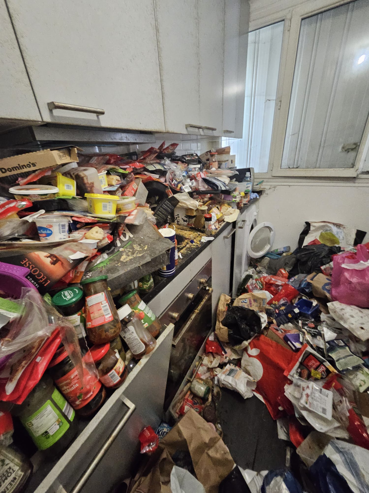 Cuisine encombrée avec accumulation de cartons et conserves