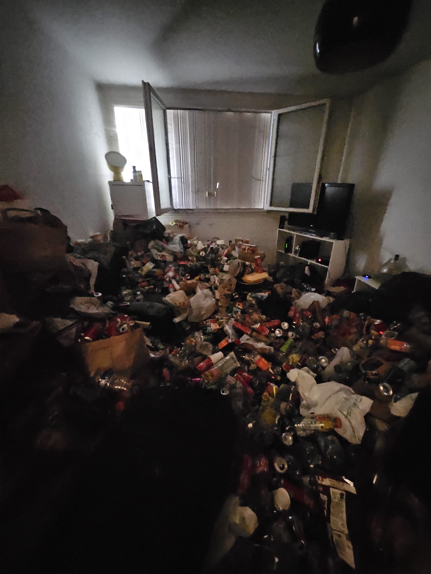 Salon avant nettoyage extrême : pièce entièrement encombrée de canettes et déchets après squat sévère